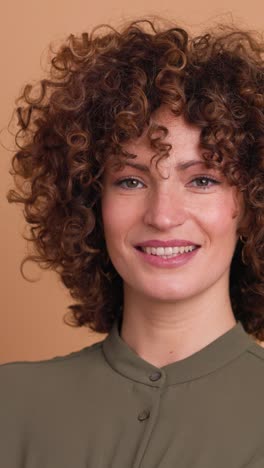 smiling standing young curly haired woman on beige background. vertical orientation