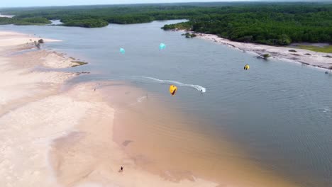 grupo de kitesurfistas montando la cometa junto a una selva en el delta brasileño