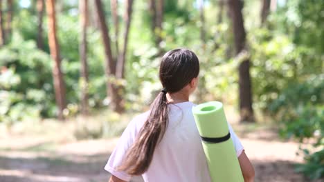 mujer caminando en el bosque con una alfombra de yoga
