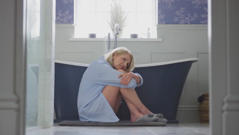 mujer madura en la menopausia que sufre de incontinencia sentada en el suelo del baño en casa