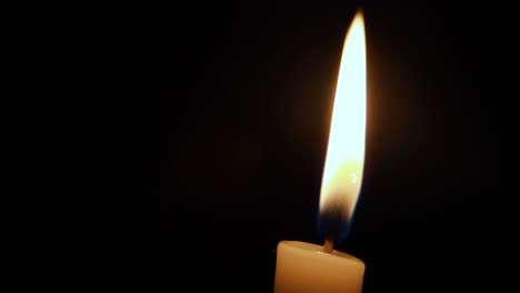 Close-up-view-of-a-candle-against-a-black-background-almost-will-with-a-soft-breeze-coming-in-making-it-move-and-settle