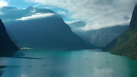 a flight over the sill turquoise waters of the norwegian loenvatnet lake with mountains towering on the sides scraping through the low hanging white clouds