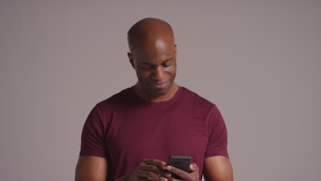 studio shot of smiling mature man with mobile phone getting good news against grey background 2