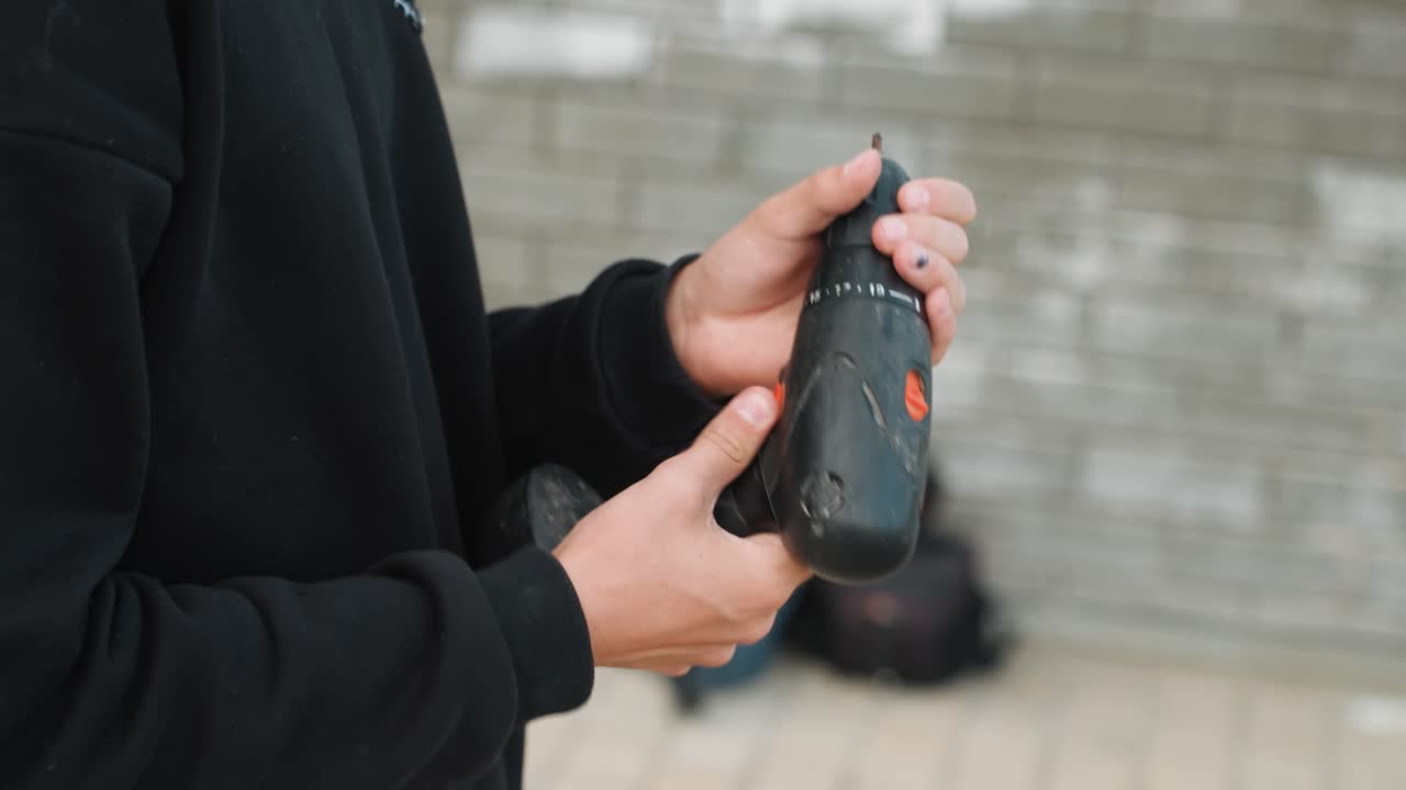 Primo piano delle mani che cambiano una punta da trapano con un'attenta ispezione, eseguendo regolazioni tattili e mantenendo un controllo stabile del polso. Questa operazione rappresenta un controllo di manutenzione concentrato in un'officina all'aperto, completato da una verifica finale della sicurezza e una calibrazione fine.