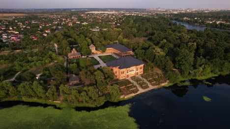 Mogoșoaia-palace-in-romania,-lush-greenery,-golden-hour-light,-tranquil-lake,-aerial-view