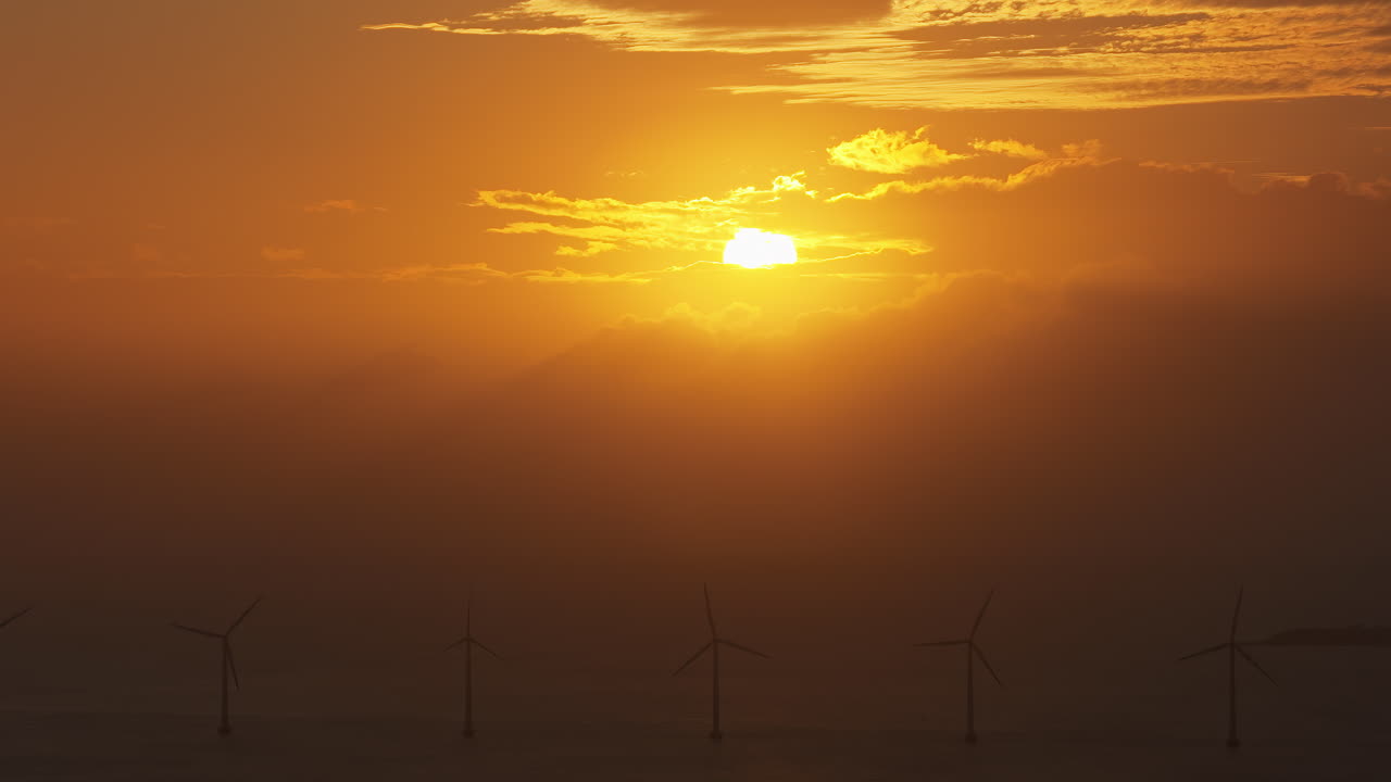 Aerial drone view of the golden sun over the Danish coast, casting light on offshore wind turbines