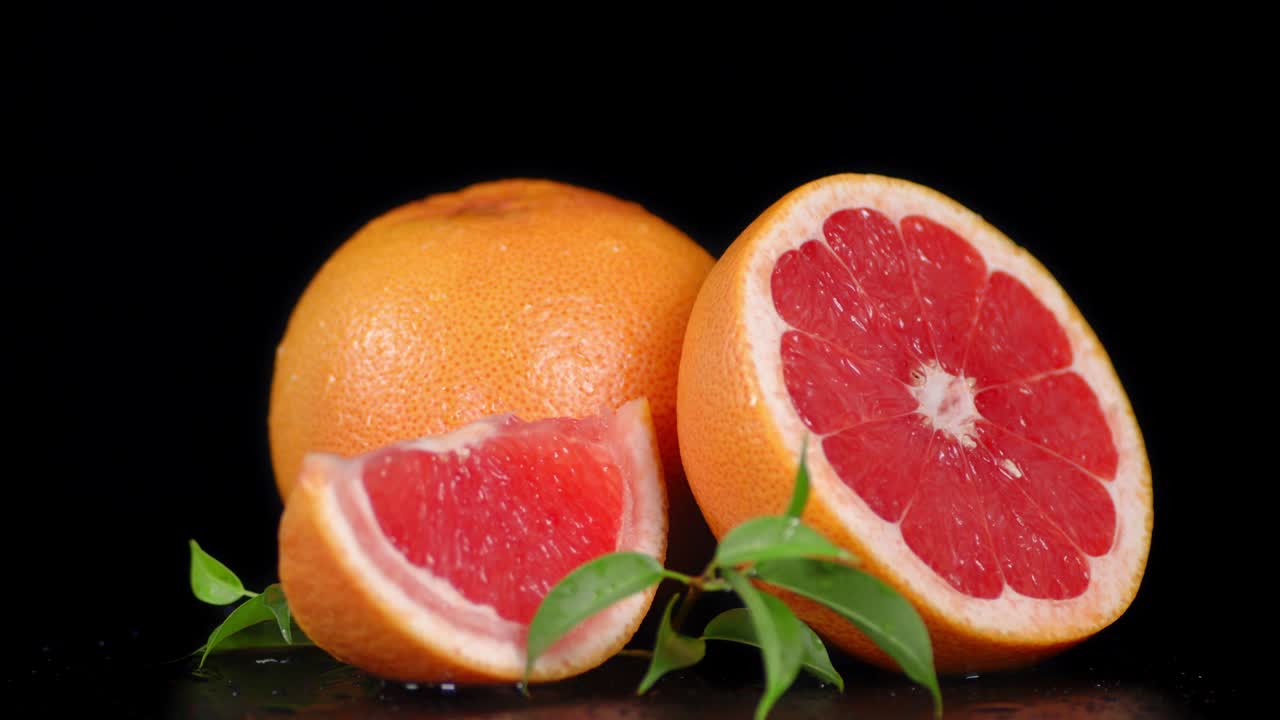 잎이 있는 익은 그레이프프루트의 조각들이 천천히 회전합니다.