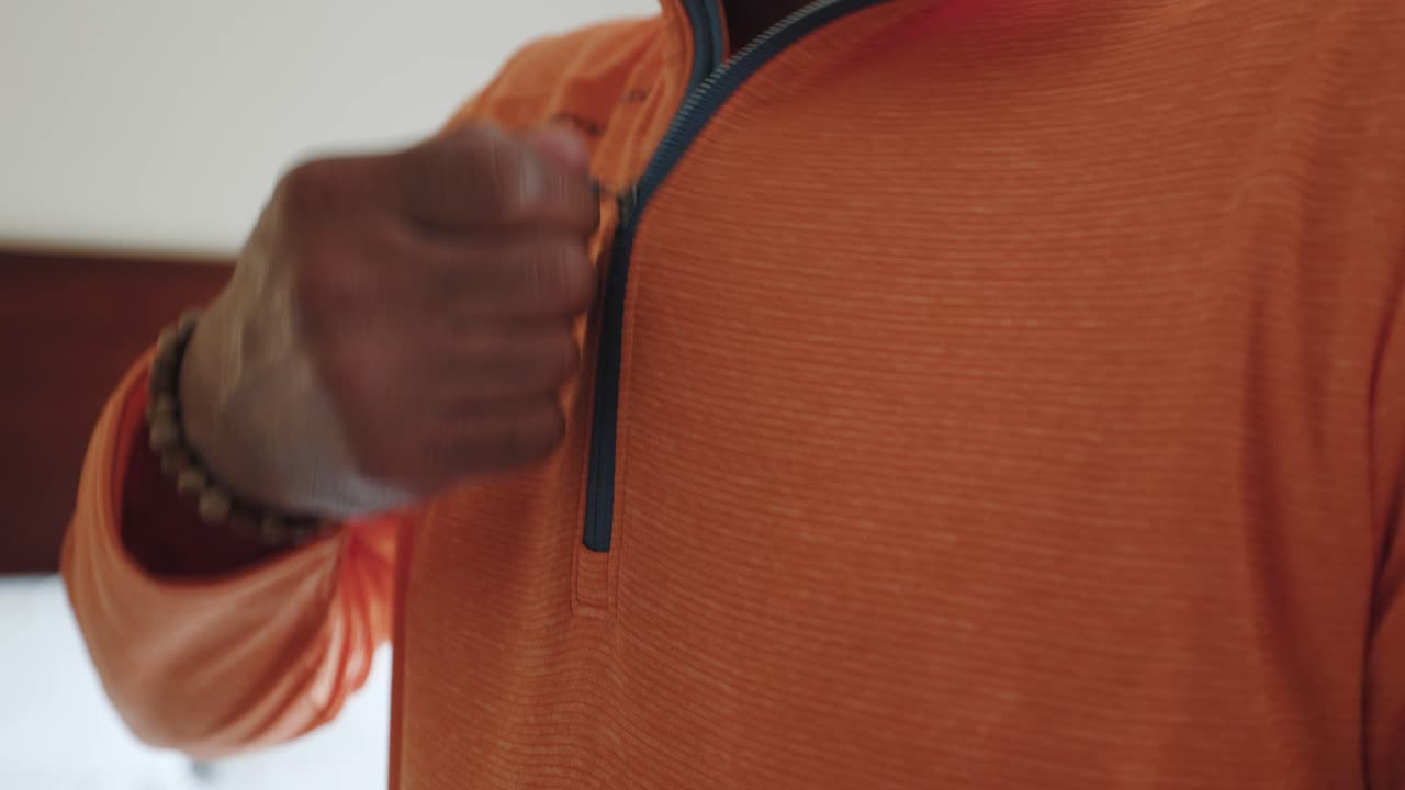 Adult Man Zips up his Windbreaker in a Brightly Lit Hotel Room