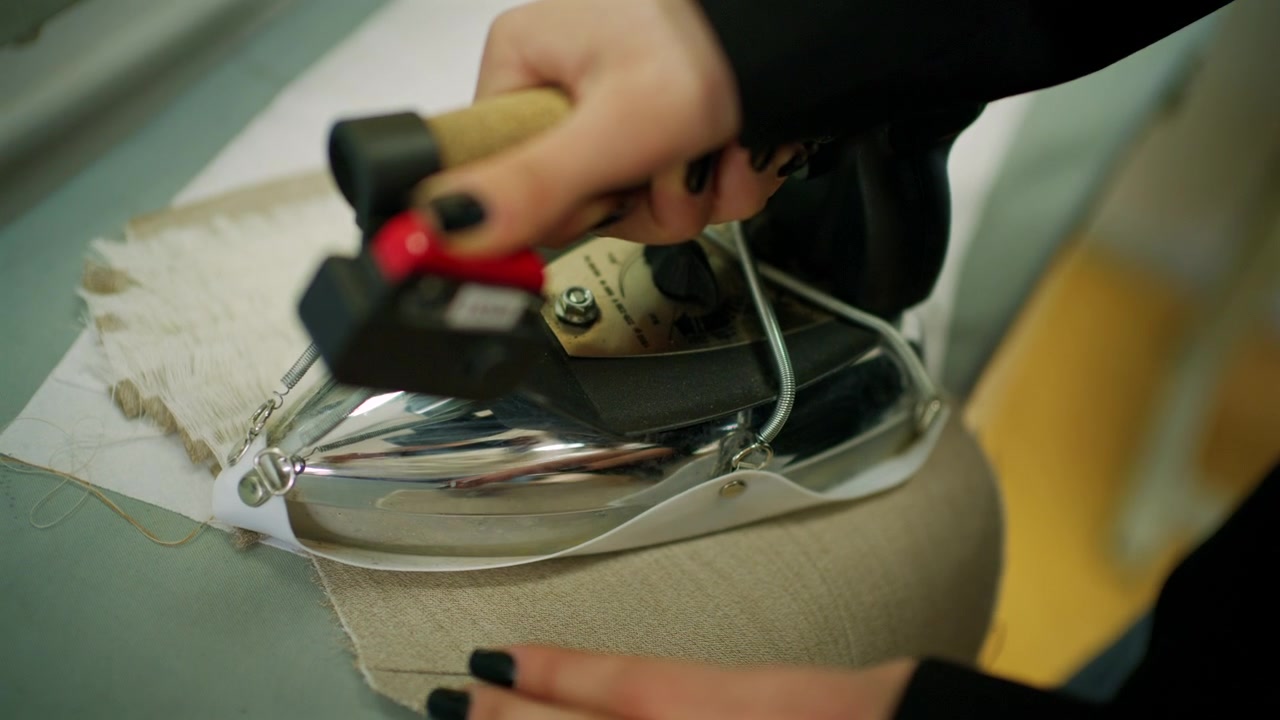 Designer's hands use a professional steam iron to press white fringed fabric on a studio table