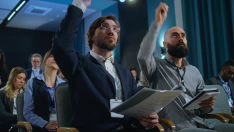 journalists sit and write answers in notebooks from politician during press campaign in the conference hall. caucasian male media representative raises his hand and asks questions during interview.