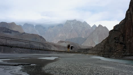 women walking across the suspension bridge of hussaini with rocky mountain ranges in background at hunza nagar, northern pakistan