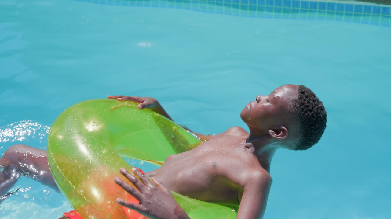 Teen male shifting weight, adjusting neon ring to relax in residential pool wearing orange trunks