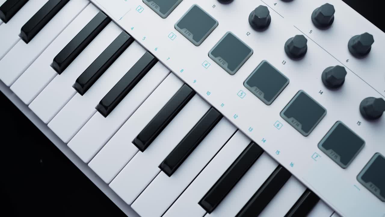 Gros plan rotatif d'un contrôleur clavier MIDI blanc avec des touches de piano, des pads et des potentiomètres sur un bureau sombre. Équipement moderne de production musicale pour home studio avec espace pour du texte.
