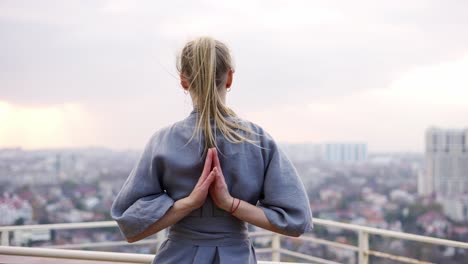 blonde woman enjoys city view and folds her hands behind back in a namaste gesture