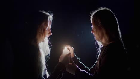 mom and daughter light a candle in the dark, look at the flame