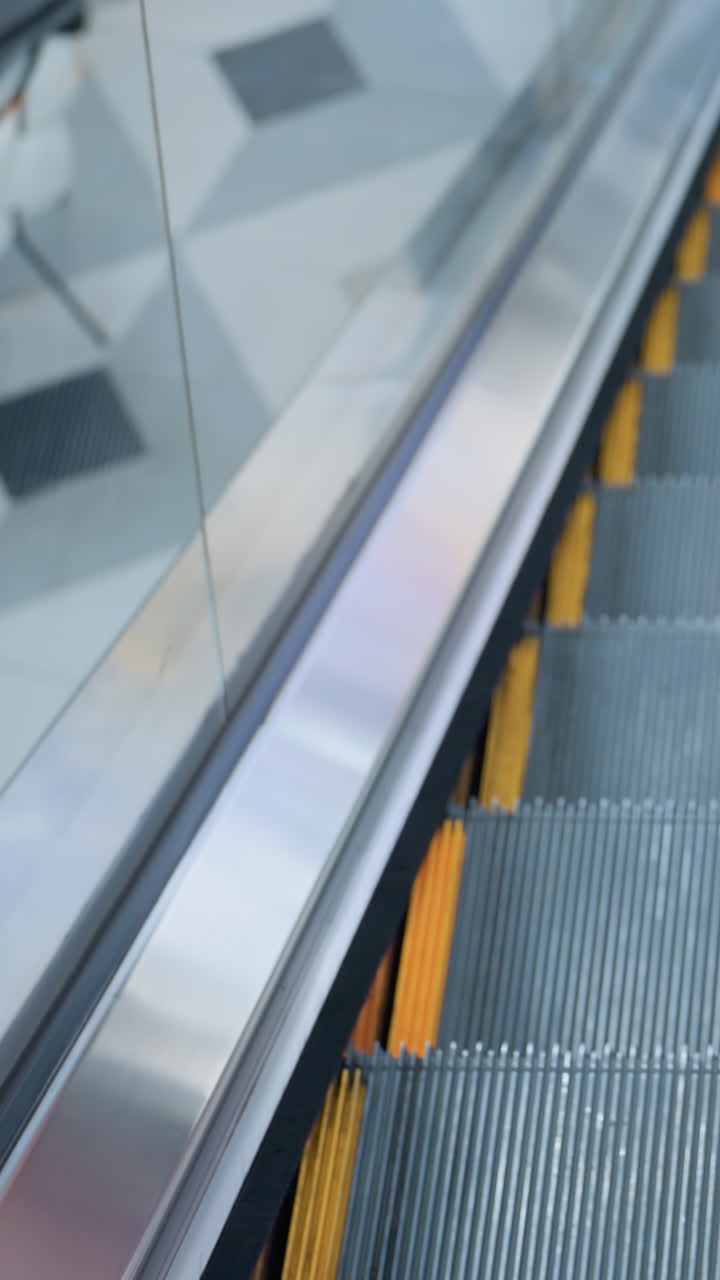 Upward-moving escalator with sleek glass frame and reflections along the border in a modern shopping mall, smooth metal steps, polished railing, and dynamic perspective