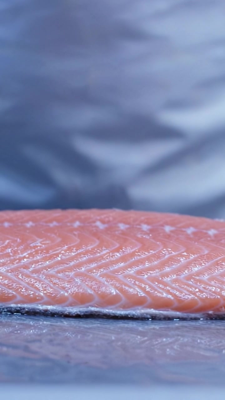 Preparazione artigianale di filetto di salmone fresco che mostra la consistenza e il colore delicati del filetto di pesce crudo, pronto per l'eccellenza culinaria nell'alta ristorazione.
