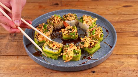 close-up of hands with chopsticks, awkwardly picking up an avocado sushi roll from a blue plate