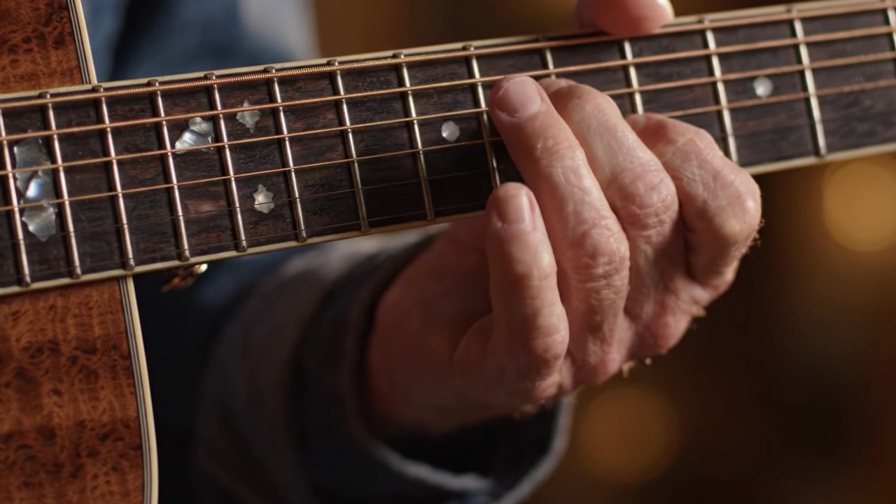 Un Primo Piano di una Mano che Suona Abilmente la Chitarra, Mostrando i Tasti e le Corde Intricate di un Bellissimo Strumento Acustico in un Ambiente Caldo e Accogliente