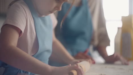 la niña está haciendo la masa diligentemente en la cocina de la casa. la madre está enseñando a su hija a cocinar comida casera.