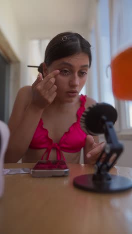 young woman applying makeup in a bikini