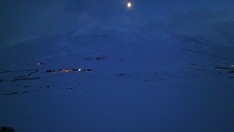 bright light above a snowy mountain in winter landscape with sporadic lighting of houses of iceland during the night