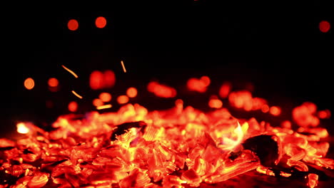 hot smoldering embers in the campfire. close up view on the glowing charcoals and tiny sparkles going up.