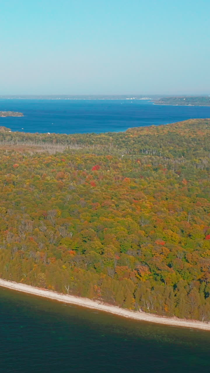Brilliant autumn foliage spreads across the Door County peninsula, meeting the calm blue waters of Lake Michigan in a seamless blend of color, texture, and natural tranquility
