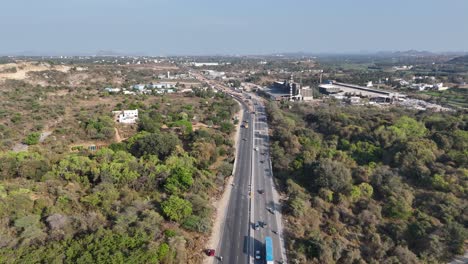 an aerial long shot captures a straight, multi-lane highway stretching into the distance through a predominantly dry, shrub-covered landscape