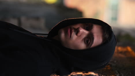 cinematic vertical portrait of handsome young man dressed in black hoodie looking aside at camera, depth of field