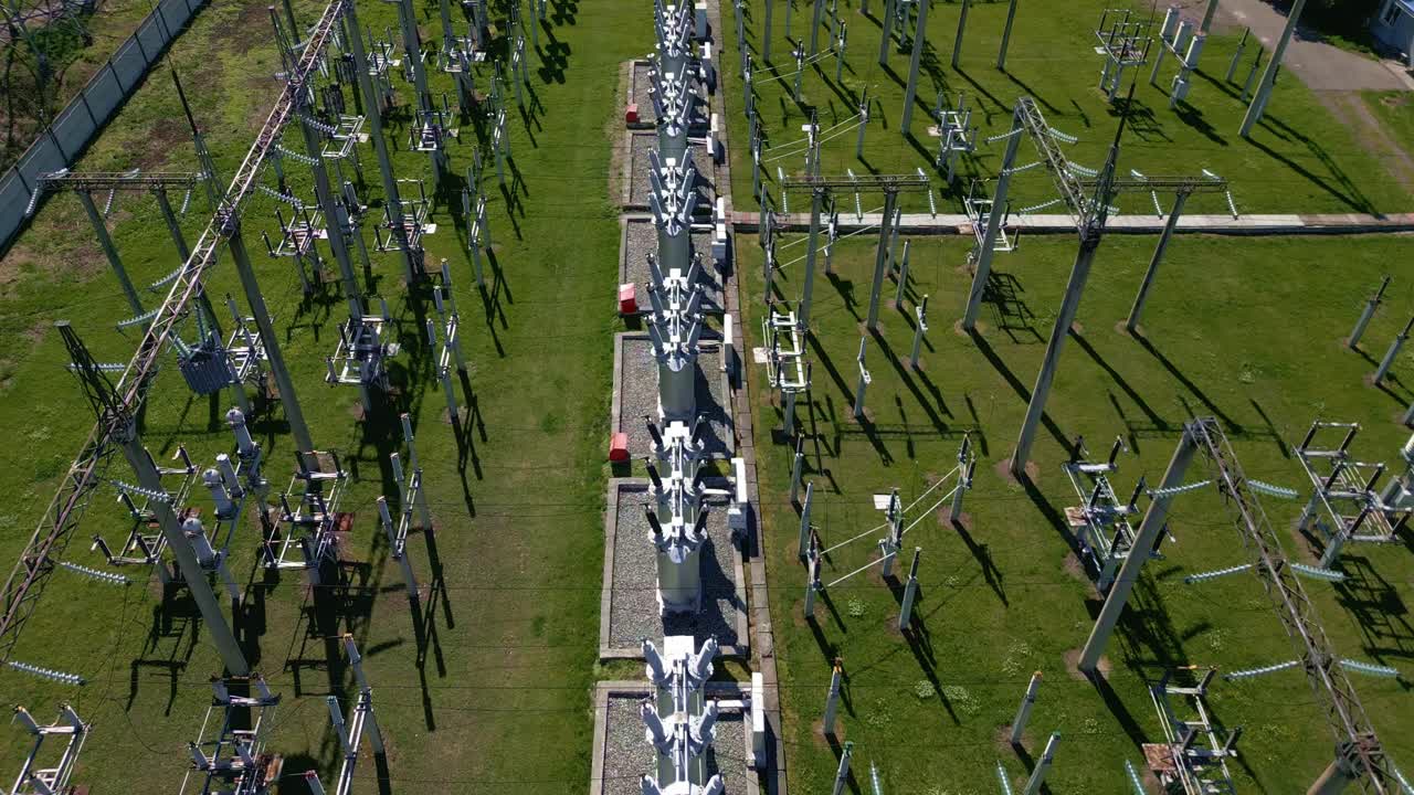 Luftaufnahme von Kraftwerksanlagen. Metallstrukturen stehen in präzisen Reihen. Grünes Gras umgibt die Industrieanlage. Lange Schatten ziehen sich über den Boden. Es sind keine Personen auf der Aufnahme zu sehen.
