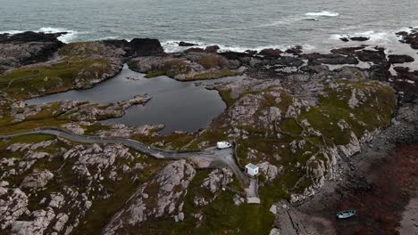 A-white-camper-van-is-parked-up-on-an-Irish-peninsula-surrounded-by-tidal-pools,-rocks-and-a-small-bay-with-a-fishing-boat