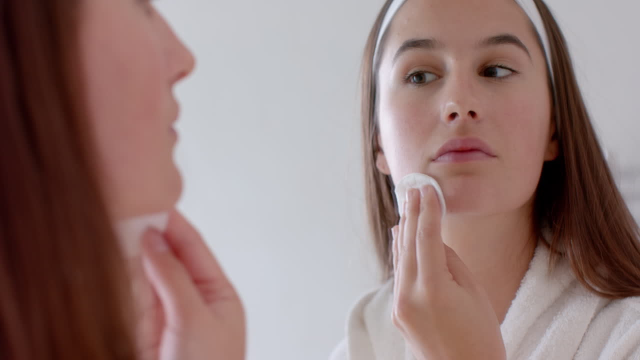 Applying facial cleanser, woman looking in mirror during home spa routine