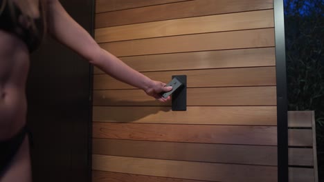 joven llega a encender la ducha al aire libre en una sauna de lujo por la noche en un bikini negro