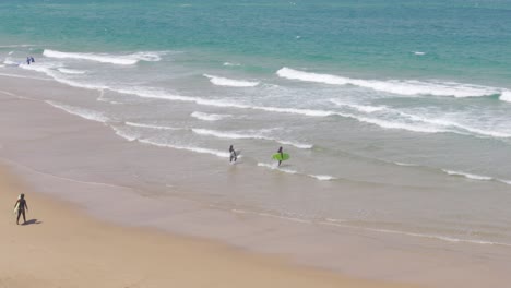 two surfers entering the water with their surfboards at praia do guincho, portugal