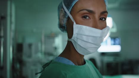 portrait of happy biracial female surgeon with face mask in operating room in slow motion