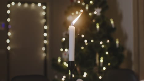 the camera focuses on a burning candle, there is a christmas tree with blurred lights in the background 1