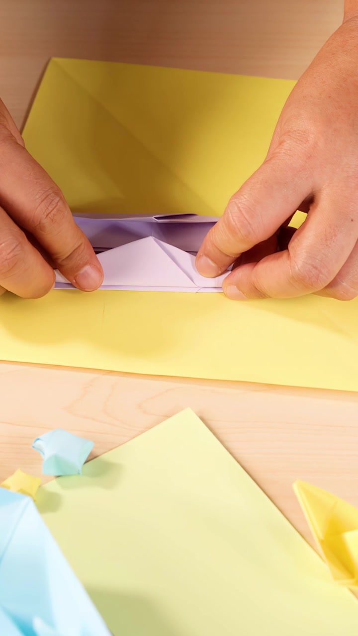 Una persona piega con cura carta origami color pastello, luce intensa, primo piano, vista dall'alto, ambiente artigianale.
