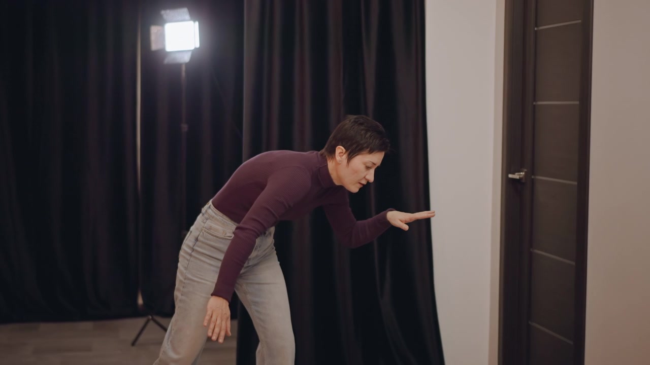Danseprøve, moderne bevegelsesklasse, gulvarbeid, to dansere øver fotarbeid og timing på studiogulvet, svarte gardiner, lyslenker, retningsbestemt lampe, instruktør observerer dynamiske positurer