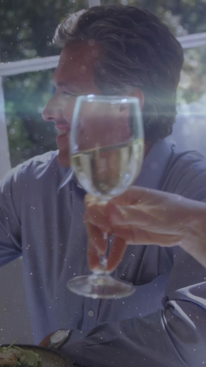 Smiling blue-shirted man watching arm reaching bringing wine glass to toast at table, salad plate