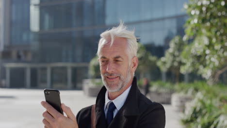 portrait-happy-mature-businessman-using-smartphone-video-chat-blow-kiss-enjoying-conversation-talking-on-mobile-phone-in-sunny-urban-city-slow-motion