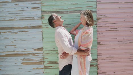 happy senior caucasian couple embracing by coloured weathered wooden wall, in slow motion