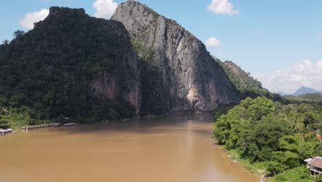 Aerial-Flying-Over-Mekong-River-In-Luang-Prabang-With-View-Of-Towering-Cliff-In-Background