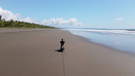 young man on scooter riding over the hard sand of a wide, long tropical beach