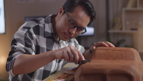 close up of asian man automotive designer works on the sculpture of car clay using rake or wire to smooth out the surface and create details in the design in the studio