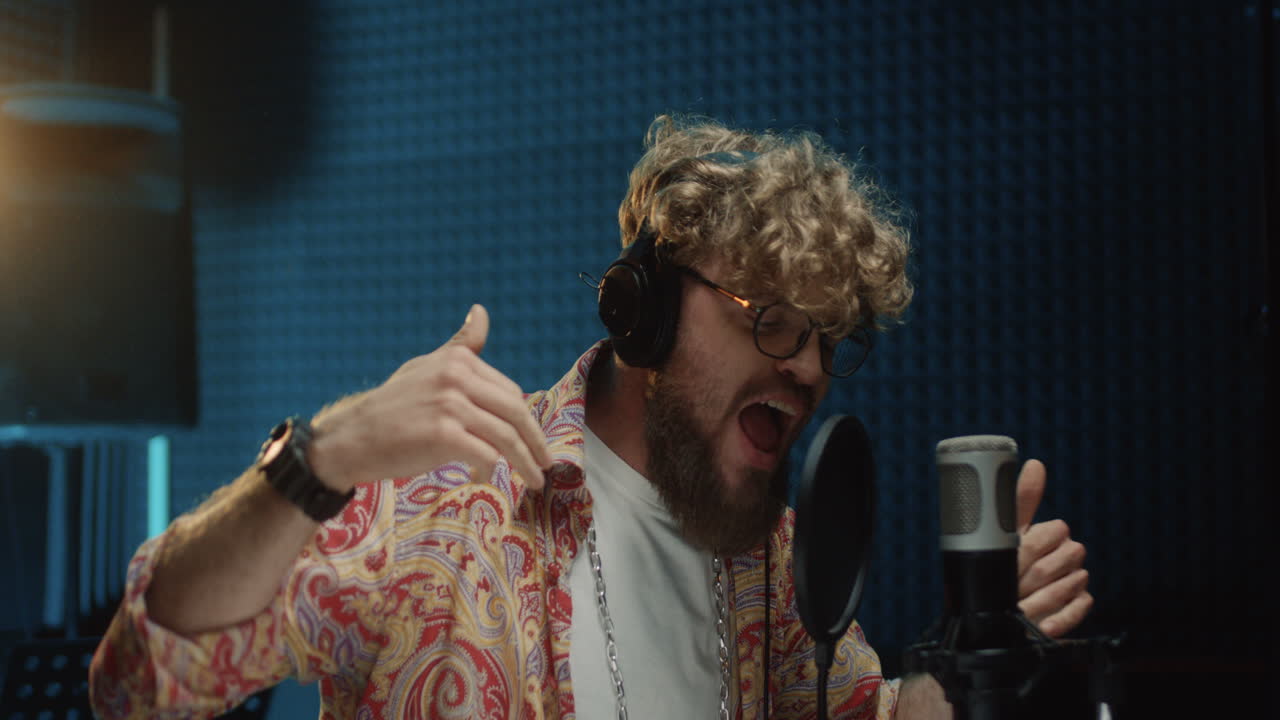 joven cantante hipster grabando una voz y cantando su canción en el micrófono en la sala de estudio de sonido