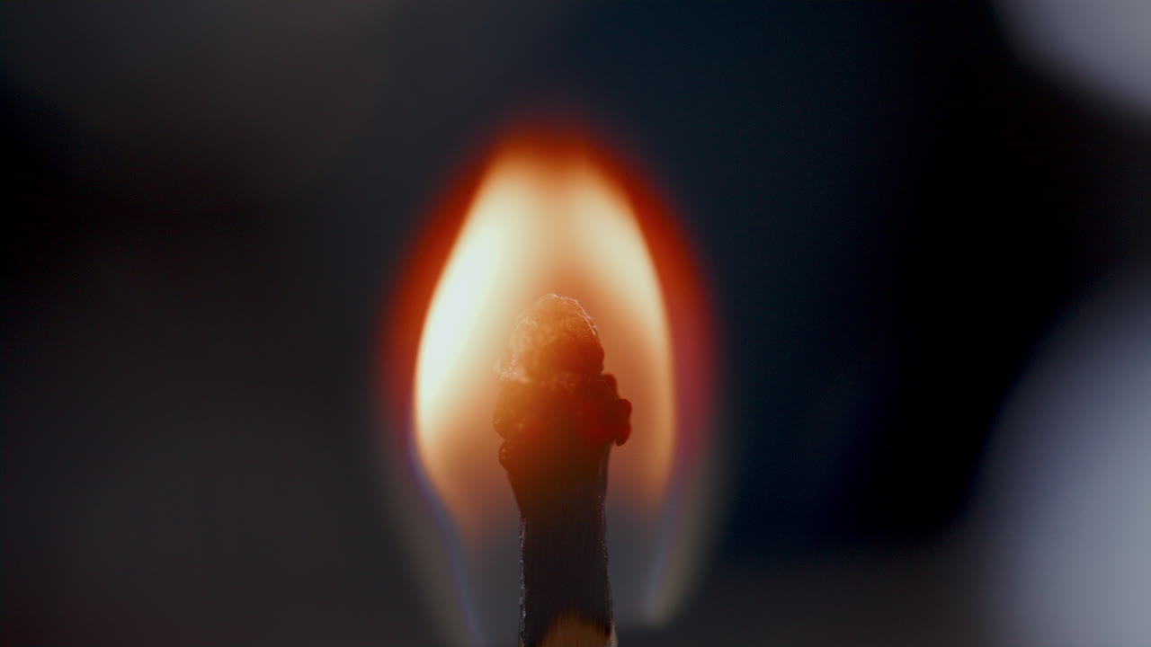 Primo piano di un fiammifero che brucia con una fiamma luminosa al buio.