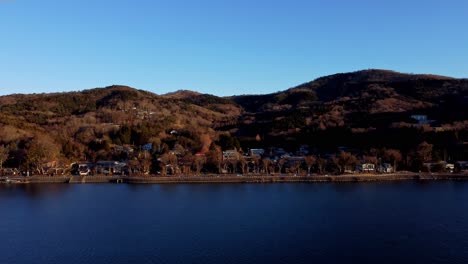 Una-Serena-Ciudad-Junto-Al-Lago-Al-Atardecer,-Con-Colinas-Al-Fondo-Y-Cielos-Despejados,-Vista-Aérea