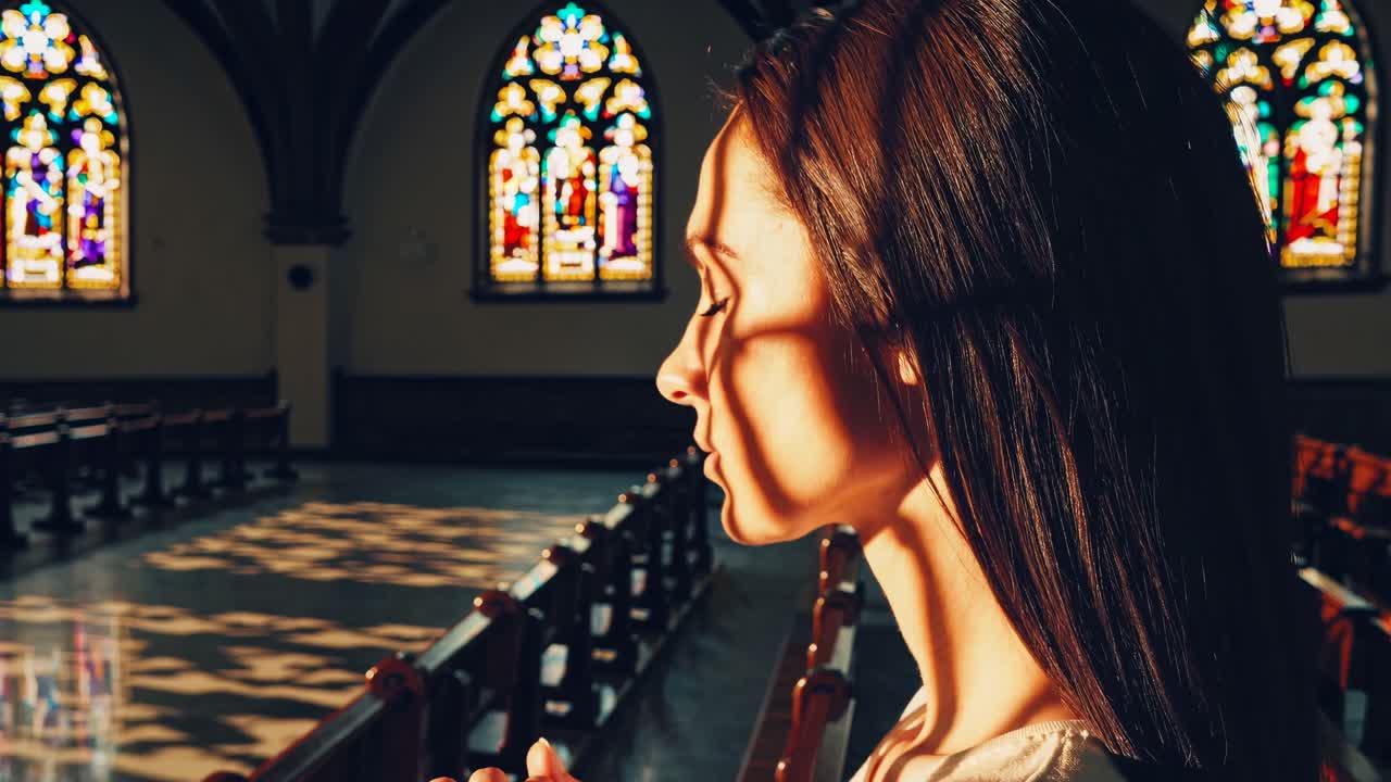 Side profile of a woman praying in a church, bathed in stained glass light