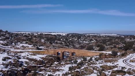 vista aérea de un dron volando sobre un hermoso campo nevado soleado con un río y un puente viejo